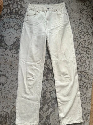 Vita raka jeans - Säljer ett par vita jeans med rak passform och hög midja. Klassisk femficksmodell med bälteshällor och knappgylf. Jeansen har en liten brun patch på ena bakfickan och är tillverkade i kraftigt bomullstyg. Modellen heter A’94 High Straight