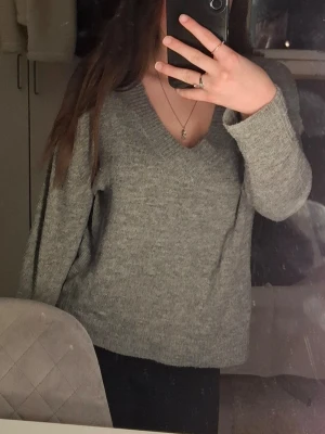 Grå v-ringad stickad tröja Amisu - Grå stickad tröja från Amisu med v-ringning och långa ärmar. Tröjan har ribbade muddar vid ärmslut och nederkant för en snygg passform.