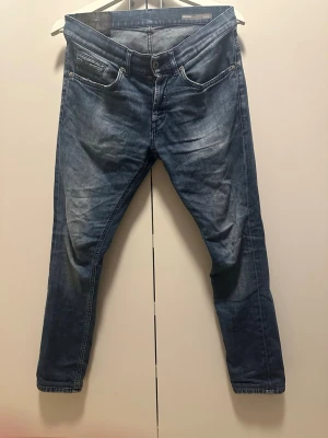 Dondup George jeans - Snygga blå slim fit jeans med lätt slitna detaljer och klassisk femficksdesign. Jeansen har en modern passform med smalare ben och subtila tvättade partier för en cool look. Perfekta för dig som gillar en avslappnad men trendig stil.