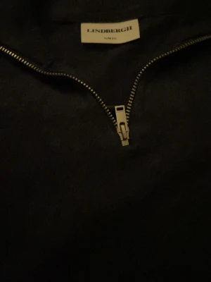 Mörkblå halvzip-tröja från Lindbergh - Mörkblå långärmad tröja från Lindbergh med slim fit-passform och halvzip-dragkedja framtill. Perfekt för en stilren och avslappnad look. Tröjan har enkel design och är lätt att matcha med andra plagg.