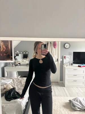 Svart långärmad topp med nyckelhålsdetalj - Säljer en svart långärmad topp med snygg nyckelhålsdetalj framtill. Toppens passform är slim och den har en enkel, stilren design som passar perfekt till jeans eller kjol. Materialet känns mjukt och stretchigt, troligen bomull eller polyester.