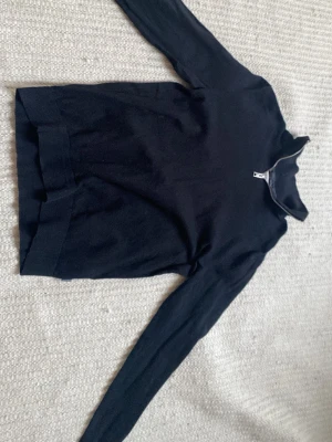 Svart tröja från Jack and Jones x -s - Mörkblå stickad tröja med lång ärm och halv dragkedja vid halsen. Tröjan har ribbade muddar vid ärmslut och nederkant samt en högre krage som kan vikas ner. Perfekt för lager-på-lager och enkel att matcha.