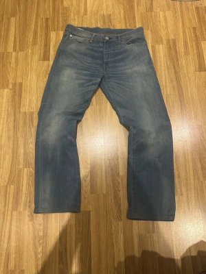 Ljusblå bootcutjeans från Levi's - Säljer ett par klassiska ljusblå jeans från Levi's med bootcut passform och fem fickor. Jeansen har slitningar och en vintagekänsla, perfekta för en avslappnad stil. Tillverkade i bomull med Levi's ikoniska läderpatch bak i midjan.