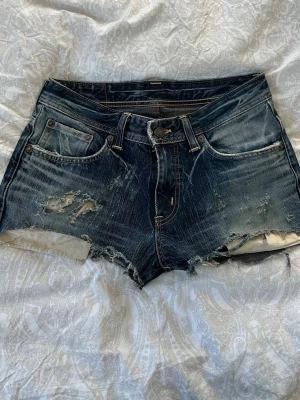 Blå slitna jeansshorts - Säljer ett par blå jeansshorts med råa kanter och slitna detaljer framtill och baktill. Omgjorda från jeans till shorts🙏🏻 Perfekta för sommaren!