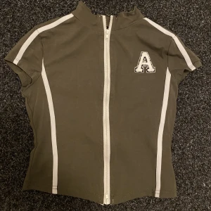 Croptop med dragkedja  - Cool grön croptop med vita detaljer och dragkedja. Aldrig använd. Strl xs/s