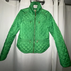 Michael kors jacka - Michael Kors grön jacka med guld detaljer. Storlek M, liten i storlek. Liten del av mörknad i tyget på armarna.