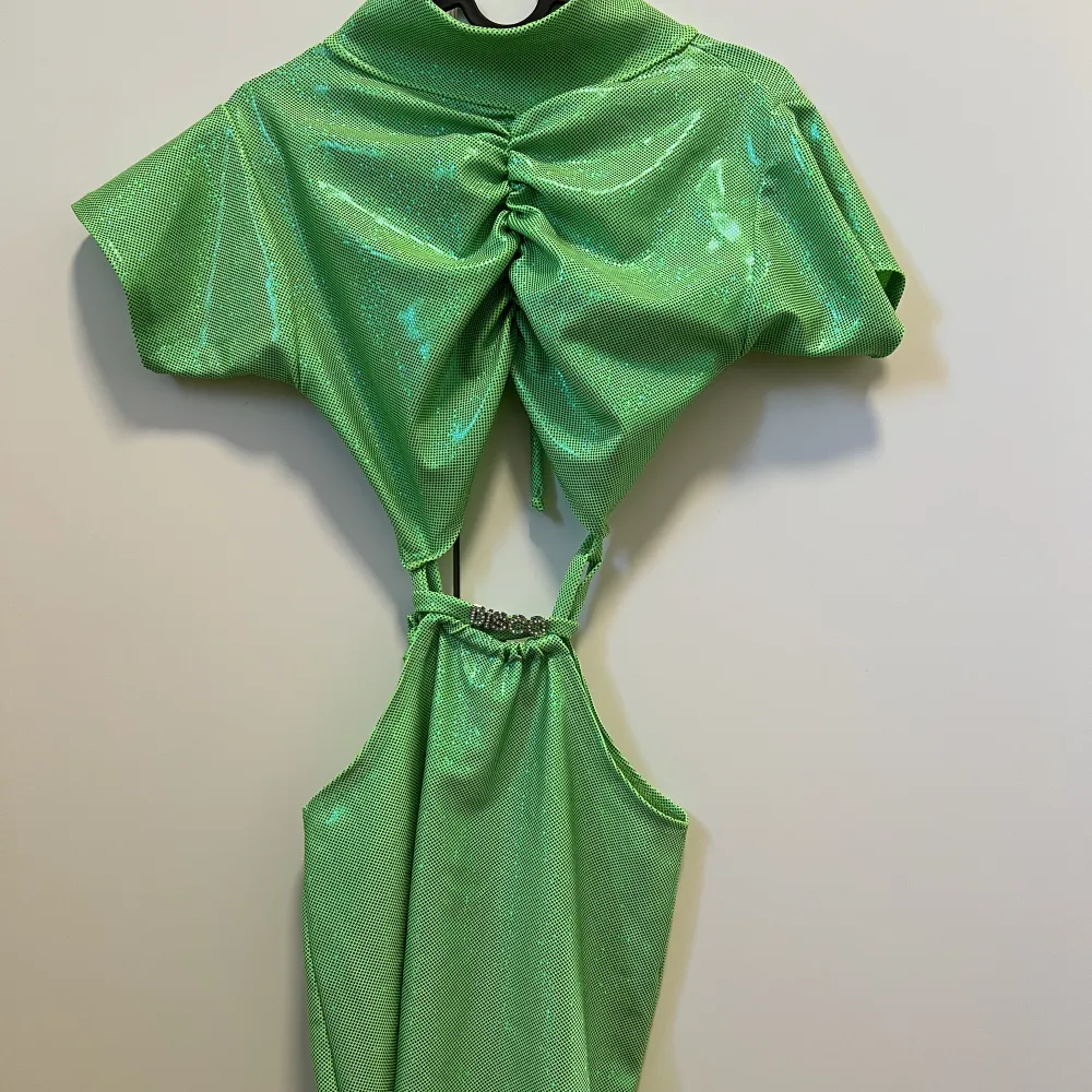 Lime grön glansig klänning från Roxanna The Label:  Rygglös, turtleneck, utskuren klänning med dragsko Tillverkad av limegrön holografisk stretchlycra Med 