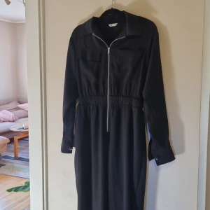 Byxdress/jumpsuit - Jättesnygg byxdress. Två fickor på bröster och dragkedja. Faller avslappnat på kroppen med markering i midjan!! Såå snygg på! Använd en gång,  nypris 599:-