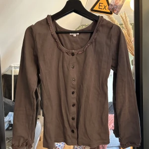 Brun Blus  - en brun blus från märket Mississippi, storlek M. Otroligt fin faktiskt, köpt i Bårlänge av alla ställen(?!) Fint skick, najs lite tjockare stretchig bomull lixsom, den sitter fint i midjan. 
