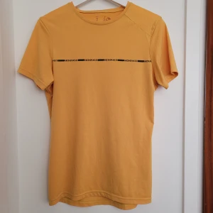 Klargul Houdini t-shirt - Klargul t-shirt som är gulare i verkligheten än hur det blir på bilderna. Litet tryckpå axeln på ryggen har lossnat lite, samma på insidan. Slitage syns på sista bilden. 