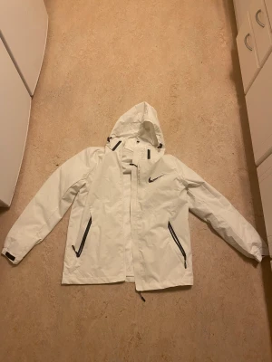 Nike regnjacka - En vit Nike regnjacka i storlek M med en luva som går att dra bort. Endast använd en gång och har en jättebra passform!