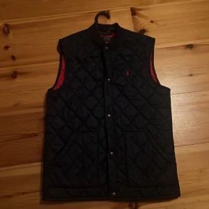 Ralph Lauren Väst  - Snygg och fräsch väst från Ralph Lauren. Använd 5 ggr. Säljer få jag inte använder den. Nyskick. Marinblå med röd innersida. Nypris 1500. Skriv gärna om frågor eller fler bilder. Kom gärna också med prisförslag 