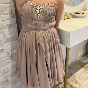 Kort festklänning med utsmyckning - Säljer en beige kort festklänning med utsmyckning uppe på klänningen. Fint skick med lite defekter och trådar som gått av, kan absolut skicka fler bilder om så önskas 💕