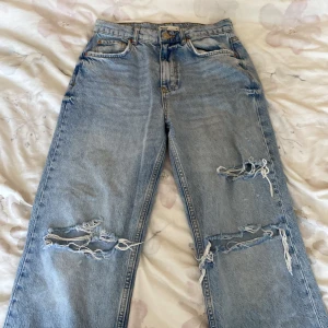 Ljusblåa jeans byxor - Dessa är byxer har två stora hål vid knäna och ett litet hål ovanpå. De är ljusblåa denim byxor som dels är baggy vid benen.