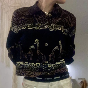 Jeansjacka motiv - Riktigt cool jeansjacka med giraff- och  leopardmönster. Bakgrunden är svart och mönstren i guld och brunt. Äkta vintage som du garanterat blir ensam om. 