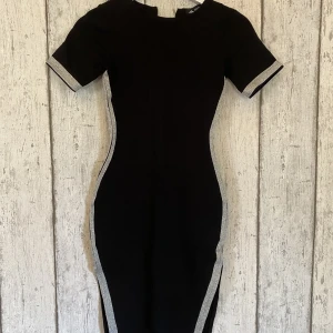 Figursydd klänning - Dö snygg svart klänning med silvriga ränder på sidorna.😍 Slits på båda sidor och en lång dragkedja i bak.  Storlek står ej, men passar någon i storlek XS eller S.  Använd vid ett enda tillfälle! Säljer för att den är för liten. 