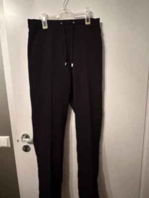 Kostymbyxor med snörning - Svarta kostymbyxor med resår band baktill, fickor samt snörning. 