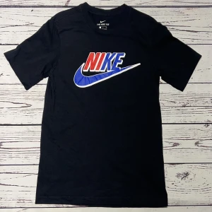 Nike T-shirt Svart (Röd/Blå) - Märke: Nike Typ: T-shirt Färg: Svart Kroppstyp: Unisex Skick: Mycket Bra  Sparande av miljö  11x lägre utsläpp jämfört med ny vara Sparat vatten ca 1850 liter Sparat CO2 ca 2.4 kg
