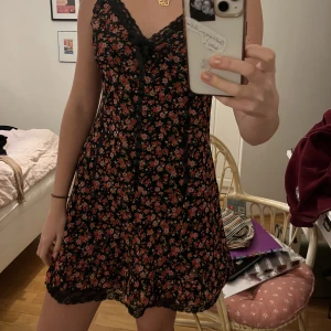 Blommig klänning med spets  - Jätte fin röd-råsa och svart, blommig klänning för sommaren, lite korset vibes på framsidan. Spets längst ner.