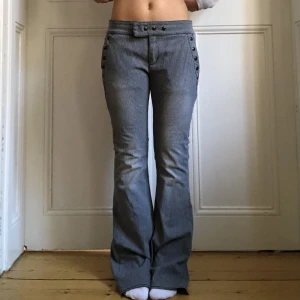 Randiga byxor  - Supersnygga blå och vitrandiga byxor från Hunkydory med runda nitar på framfickorna! Lågmidjade pch utsvängda. (Sista bilden visar färgen bäst) Midjemått: 80cm Innerbenslängd: 81cm Knappen som ska sitta längst fram på midjan har tyvärr lossnat:/ Annars br