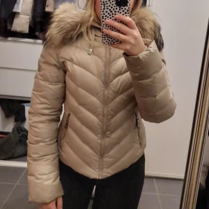 Hollies dunjacka - Beige dunjacka från Hollies i använt skick, lite missfärgad på undersida ärmarna (fråga om bild). Säljer den då jag inte använder den längre. Nypris var 3200kr.