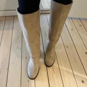 Knähöga stövlar - Knähöga stövlar i beige mocka från HM i storlek 37 (normala i storlek) Köptes för 799kr endast använda 2 ggr så mycket fint skick. Klackhöjd 7cm.