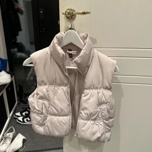 Pufferväst - En kort pufferväst med ståkrage samt dragkedja och stolpfickor fram. Fodrad.