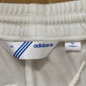 adidas byxor  - Vita addidas byxor med sliver/grå strimor på sidorna. 100% polyester 