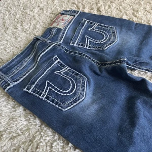 True Religion Jeans - Säljer mina True Religion jeans. ❤️ Lågmidjad och straight/smått bootcut modell med snygga vita stygn. Storlek 30 (Amerikansk strl) men passar mig perfekt som vanligtvis har 26/27. Innerbenslängd: 78,5cm. Midjemått: 35,5cm. Köpare står för frakt! 💞