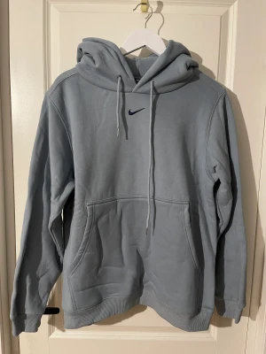 Blå nike hoodie - Blå Nike hoodie med enkel logga på bröstet. Extremt skön och bekväm. Aldrig använd. Storlek M. Sista bilden är samma hoodie fast grå. Finns även i svart och grå.