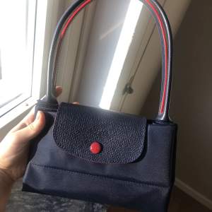 Oanvänd äkta Longchamp väska i vattentätt material med chic detaljer i marinblå och röd! 