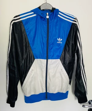 Adidas vindjacka stl S - Vintage Adidas trackie jacka storlek S med 2 hål på baksidan av höger ärm - se bilder. Bröstvidd ca 102 cm, passar S och mindre M utan problem!