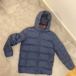 Tommy Hilfiger jacka - Dunjacka. Varm och skön på vinter. Passar båda tjejer och killar. Har inte kommit till mycket användning då jag har andra jackor som jag har haft på mig. Den har färgerna marinblå. Skriv till mig om du har frågor eller om fler bilder.
