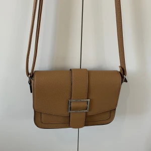 Brun väska  - Brun väska med silver detaljer, i fint skick.  20cm bred, 15cm hög.  Nypris 249kr 