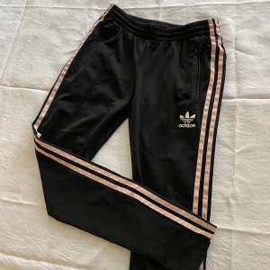 Svarta och rosa Adidas byxor - Väldigt cute svarta Adidasbyxor med rosa streck. Blixtlås längst ner på benen så man kan ha dom lite mer loose där om man vill. EU 34, UK 8 🎀