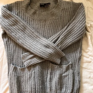 Grå stickad tröja med fickor - Grå tjockstickad tröja med fickor på magen. Fin för hösten eller kalla sommarkvällar. Se passform på bilderna jag är 177. 
