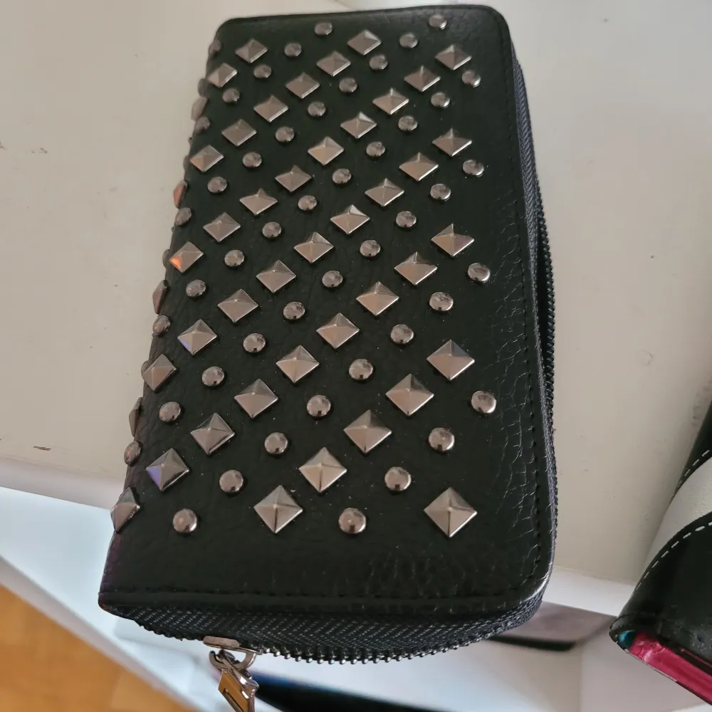Större plånbok med nitar där det kan få plats mobil i. Sparsamt använd.  Storlek 20 × 10 cm. Väskor.
