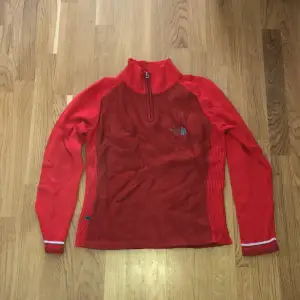 Röd tröja från The North Face med dragkedja i halsen. 50% ull 50% akryl. Står dam L på lappen men sitter kanske mer som en M.