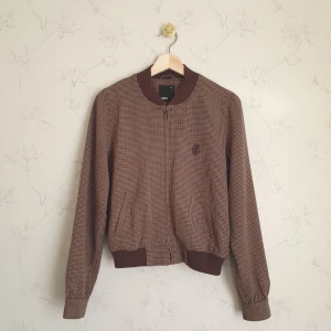 Brun bomber jacka - 🤎FÖRST TILL KVARN!🤎 Choklad brun bomber jacka med lappade armbågar för en vintage look. Jackan är även rutig  i flera bruna nyanser med ett broderi över vänstra bröstkorgen. Storlek 38, med arm muddar, rund krage. Vill bli av med ASAP!🤗