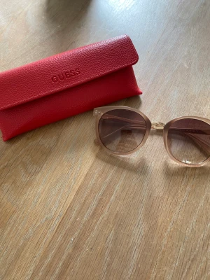 Solglasögon Guess - Fina solglasögon med ljusare glas.  Färgen på skalmen är ljus kola.  Mkt fint skick 