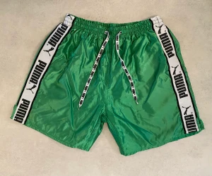 Gröna vintage Puma shorts - Gröna glansiga Puma shorts från 90-talet i använt skick, trasig innerbyxa och tråddrag förekommer men bra helhetsintryck 