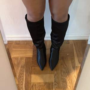 Svarta knähöga boots i satin. Användna en gång.  Köpta för ca 600kr. Klackhöjd: 9,5cm Bred passform.