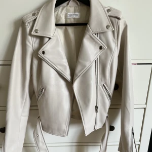 Vit skinnjacka  - En superfint vit skinnjacka från Nelly. Har ett bälte längst nere på jackan + en massa andra fina detaljer. Använd ett fåtal gånger. Storlek 36 men passar 34 också!🤗