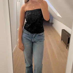 Glittrig festtopp - Säljer en glittrig svart festtopp med paljetter. Den är bandeu och har en dragkedja där bak. Paljetterna är inte blåa, bara ljuset! Köpt i en butik i Spanien för 25 euro! Perfekt till nyår, fester eller liknande!