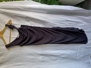 Svart klänning - Kort klänning m slits, mjukt matrial, strech, tunna axelband, tyg blommor som dekorerar vid ena axeln å vid slits, helsvart, köpt för många år sedan, inte använd på länge