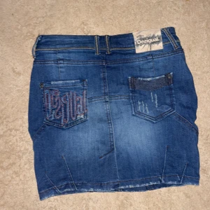 Desigual jeanskjol - Desigual jeanskjol, aldrig använd av mig då den är för liten, köpt på secondhand och står ingen storlek men den passar 28/S och är i nyskick Den har ett litet slit där bak vid rumpisen