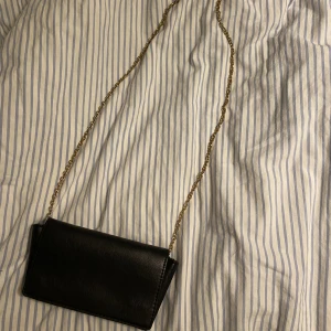 Väska - Supersnygg väska från Åhléns med inbyggd korthållare. Väskans axelband är en löstagbar guldkedja. Jag får plats med min mobil och några fler småsaker i den.