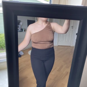 One shoulder-topp - Brun one shoulder-topp från Boohoo i storlek 34. Body-modell med tre knappar. Stretchigt och skönt material. Oanvänd!