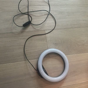 Ringlampa från Denver med USB - Säljer en rund ringlampa från Denver med vit ram och svart fäste. Lampan har USB-anslutning och en kontroll på sladden för att justera ljusstyrka och färgtemperatur. Perfekt för sminkning eller content creation. Aldrig använd. Orginal pris ca 300kr. Pris kan diskuteras!