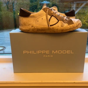 Vita sneakers från Philippe Model - Säljer ett par vita Philippe Model PRSX Low Man sneakers med grå detaljer och snörning. Skorna har en klassisk rund tå och platt sula. Märket syns tydligt på sidan och tungan. Perfekta för dig som gillar stilrena sneakers.